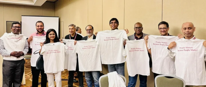 A group standing in a meeting room holding up printed T-shirts