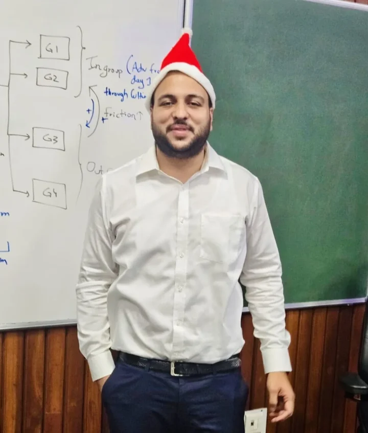 Standing in front of a blackboard wearing a festive hat