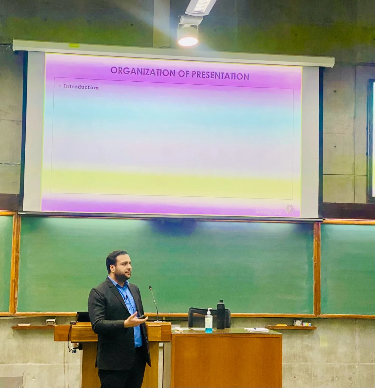 Presenting at a lectern in a lecture theatre beside a slide reading Organization of Presentation