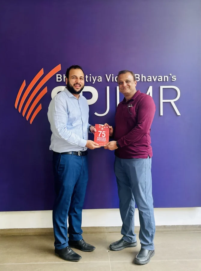 Two people holding a book in front of an SPJIMR backdrop