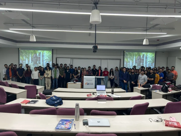 A cohort standing together at the back of a classroom