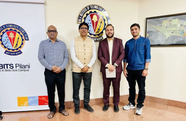 Four people standing together beside a BITS Pilani banner