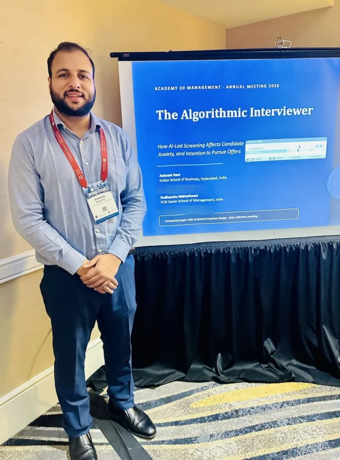 Standing beside the title slide for the paper 'The Algorithmic Interviewer: How AI-Led Screening Affects Candidate Anxiety, and Intention to Pursue Offers'